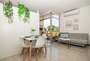 A modern living room with a dining area, a grey sofa, and a view of the outdoors. - Modern Retreat with Pool, Gym and Private Balcony (Asunción)