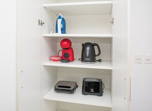 A white shelf with a kettle, a red coffee maker, a toaster, and a blue bottle of detergent. - Modern Retreat with Pool, Gym and Private Balcony (Asunción)
