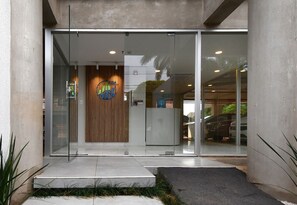 Entrada moderna de un edificio con puertas de vidrio, un mostrador de recepción y un panel de pared de madera.