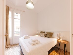 Una habitación de hotel con cama, mesita de noche, lámpara y ventana con cortinas.