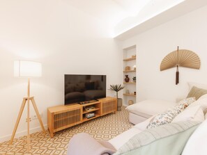Ein modernes Wohnzimmer mit Fernseher auf einem Holzständer, einer Stehlampe, einem Sofa und einem Wandventilator.