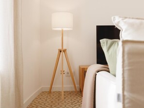 Una habitación con una lámpara de pie, una cama con almohadas y una pequeña mesita de madera.
