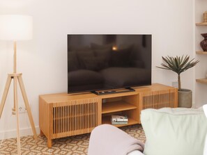 Una sala moderna con un televisor de pantalla plana sobre un soporte de madera, una lámpara de pie, una planta en maceta y una alfombra estampada.