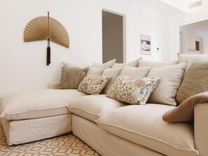 Ein beiges Ecksofa mit vielen Kissen, ein Wandventilator und ein gerahmtes Bild an der Wand.