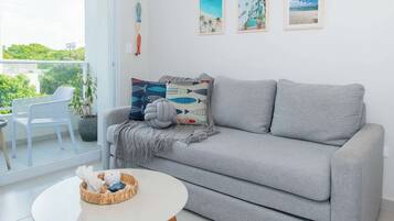 Una sala de estar moderna con un sofá gris, una mesa de centro redonda y vistas al exterior con vegetación.