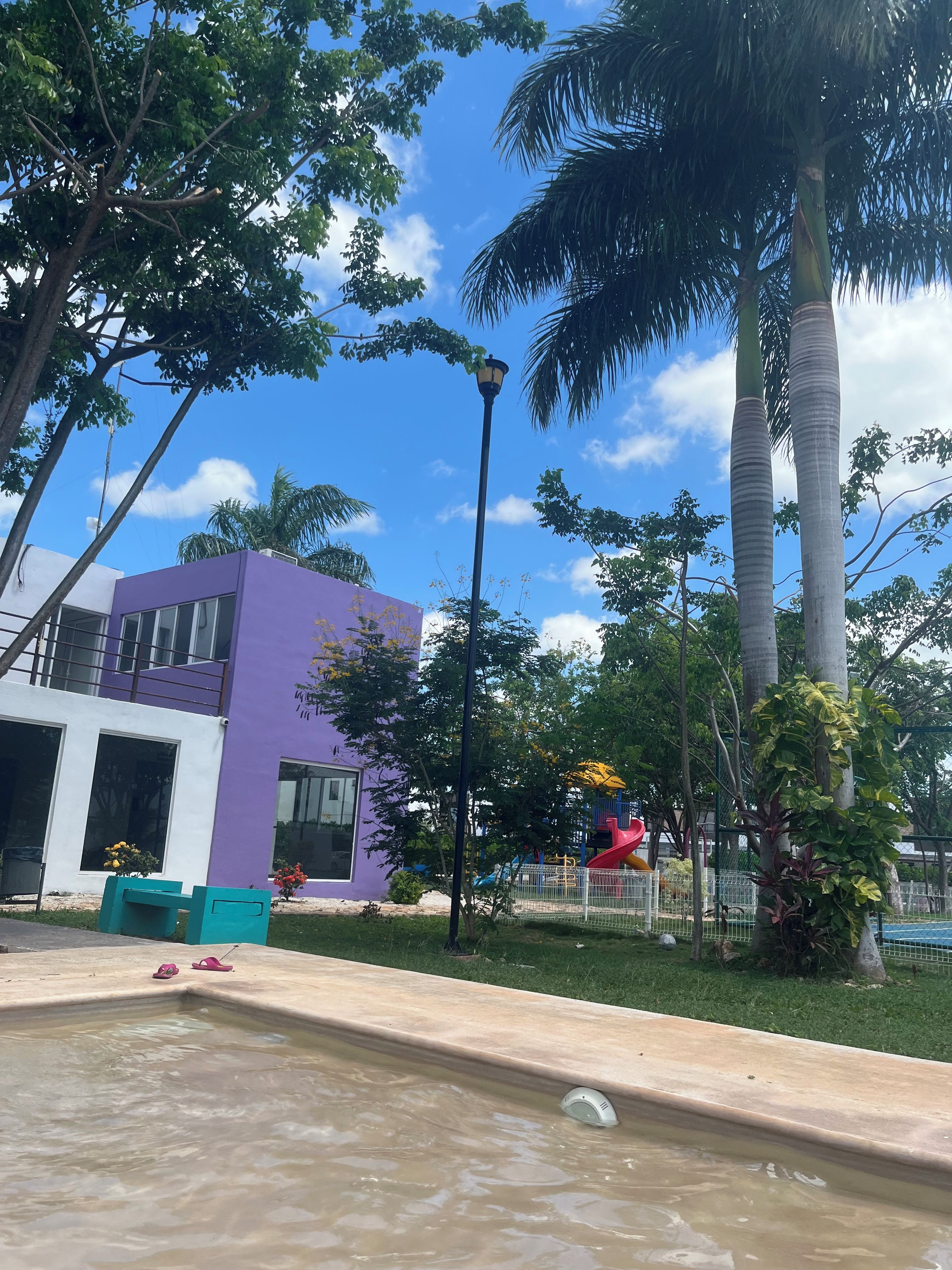 A building with a purple facade, a playground with a red slide, and a water feature.