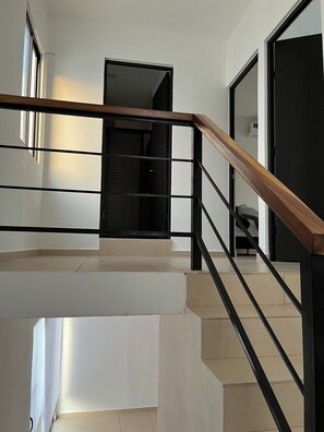 Un escalier avec une main courante en bois et des balustres en métal noir, menant à un palier.