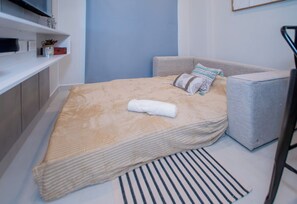 A bed with a beige cover, a white towel, and a striped rug. - Spacious 1BR | 60m², Rooftop Pool & Workspace (Fernando de la Mora)