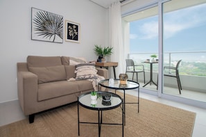 A modern living room with a sofa, two glass tables, and a balcony with a view. - Modern 1BR in Recoleta | City Views & Rooftop Pool (Asunción)