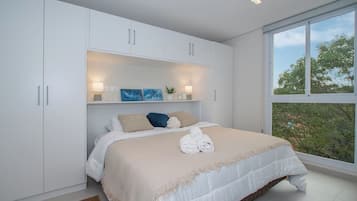 Een slaapkamer met een groot bed, witte kasten, een raam met uitzicht en een plank met decoratieve objecten.