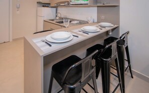 Et moderne køkken med en bar, udstyret med køleskab, vask og mikroovn. To barstole og et spisebord dækket med tallerkener, bestik og glas.