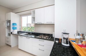 Ett modernt kök med vita skåp, en svart bänkskiva, en vattenautomat, en kaffebryggare och ett fönster med utsikt över staden.