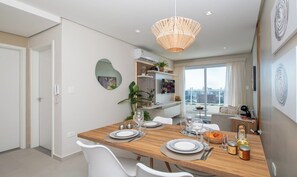 A modern dining area with a wooden table set for four, white chairs, a hanging light fixture, and a city view through large windows. - Stunning Hub with City Views, Pool and Balcony (Asunción)