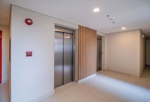 Passadís amb dos ascensors, detector d'incendis i un mur amb panells de fusta.