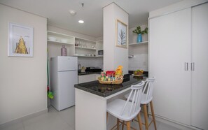 Cuina moderna amb armaris blancs, tauleig de granit i una illa central amb tamborets.