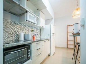 Eine Küche mit Mikrowelle, Backofen und Kühlschrank. Es gibt eine geflieste Spritzschutzwand und eine Pendelleuchte.