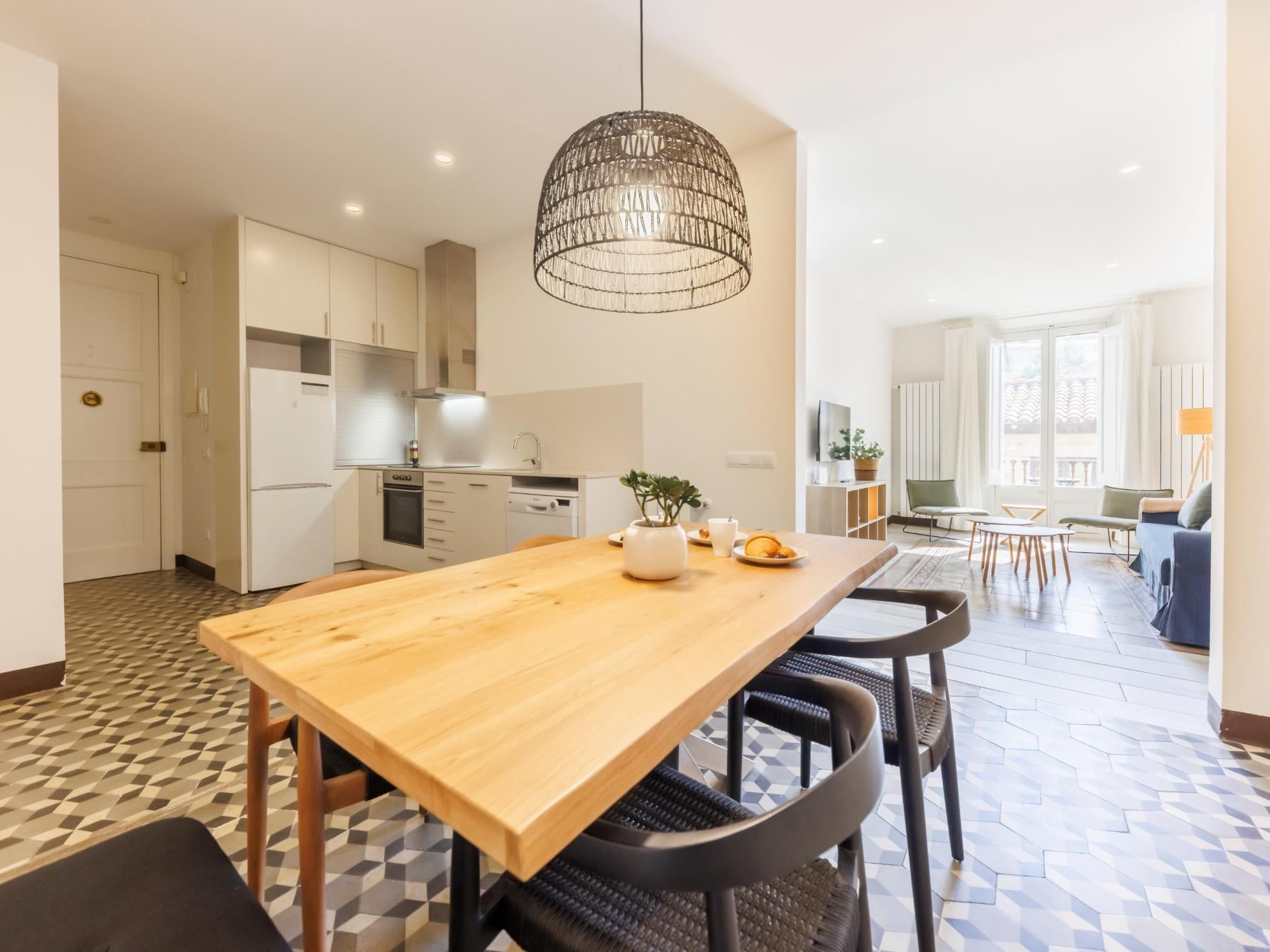 A modern kitchen with white cabinets, a wooden dining table, and a hanging light fixture.