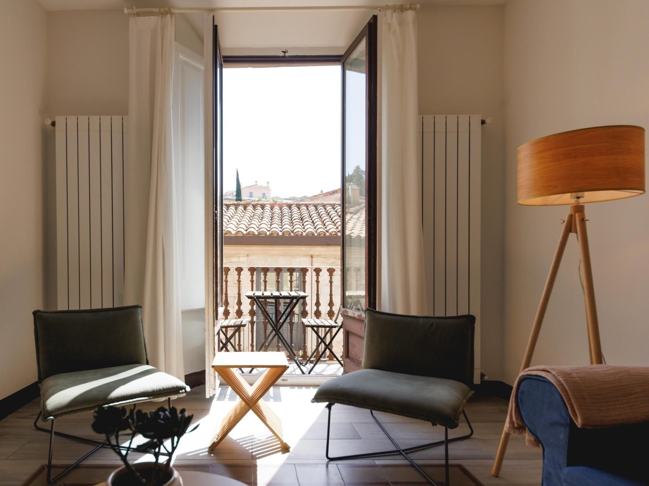 Ein Zimmer mit einem Balkon, einem Tisch, zwei Stühlen, einer Stehlampe und einem Blumentopf.