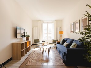 Ein Wohnzimmer mit einer Couch, einem Fernseher, Holzregalen und einem gemusterten Teppich.