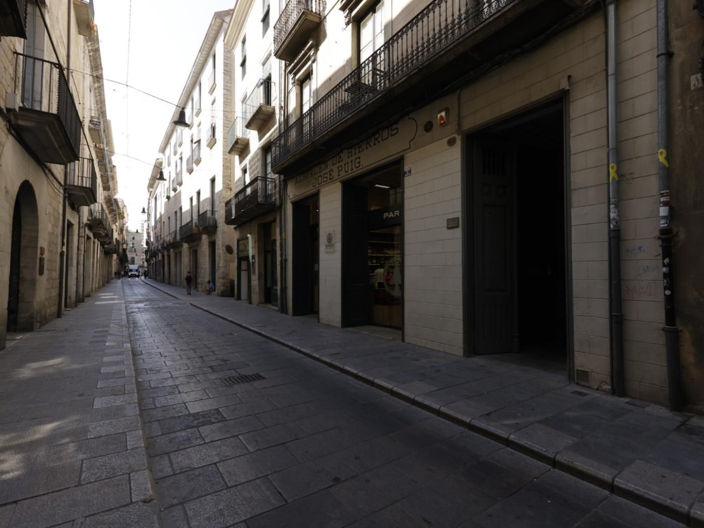 A narrow street with buildings on either side, some with visible storefronts and signage.