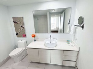 A modern bathroom with a white sink, a toilet, a large mirror, and a vase with flowers. - 1BR- Intracoastal & Marina - Private Balcony (Hallandale Beach)