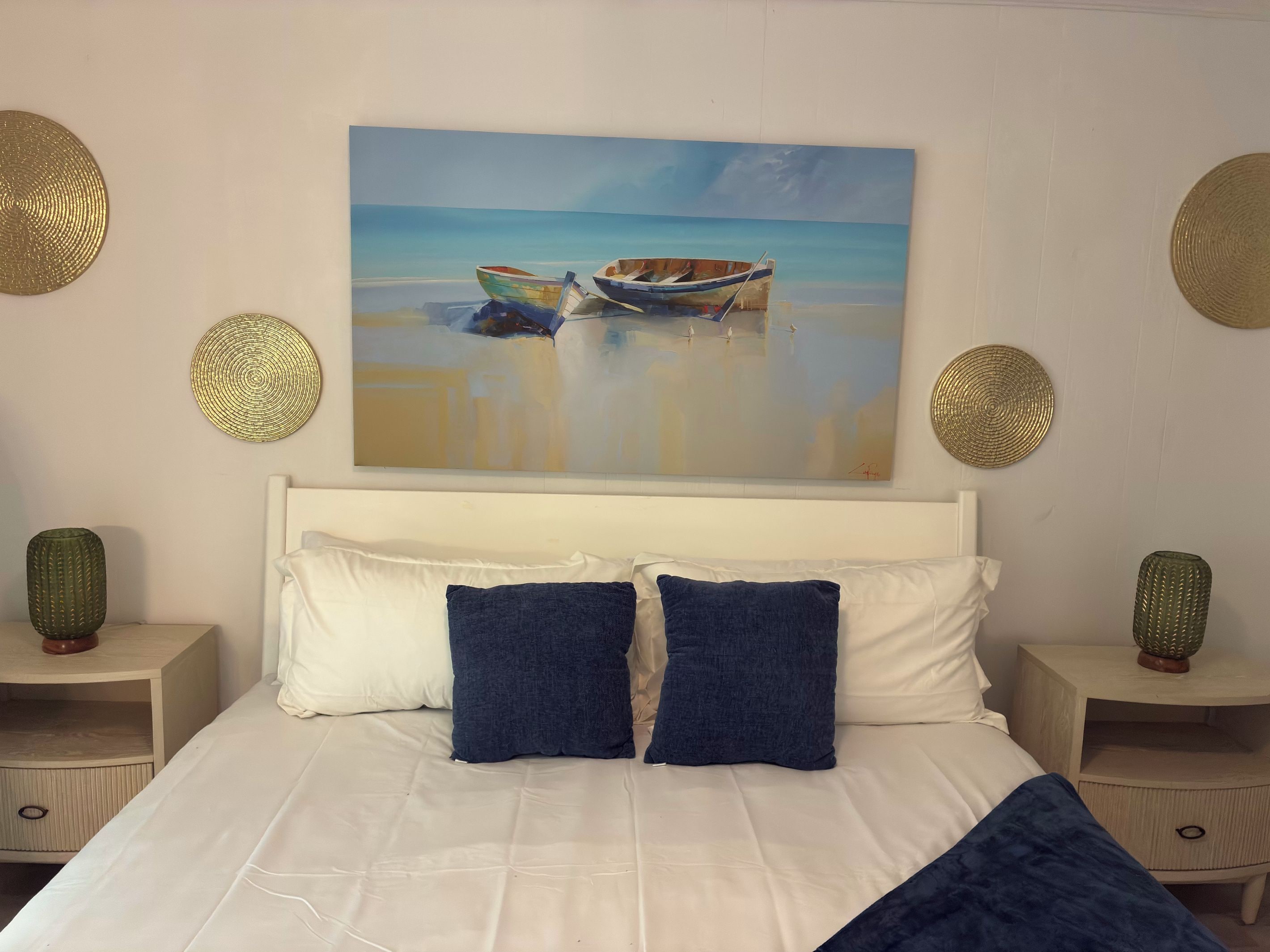 A bedroom with a large bed, two nightstands, and a painting of boats on the wall.