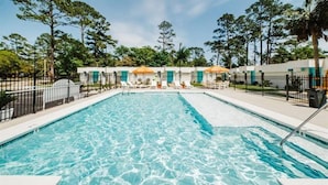Una piscina rettangolare con acqua cristallina e blu, circondata da un solarium bianco e una recinzione in metallo nero.