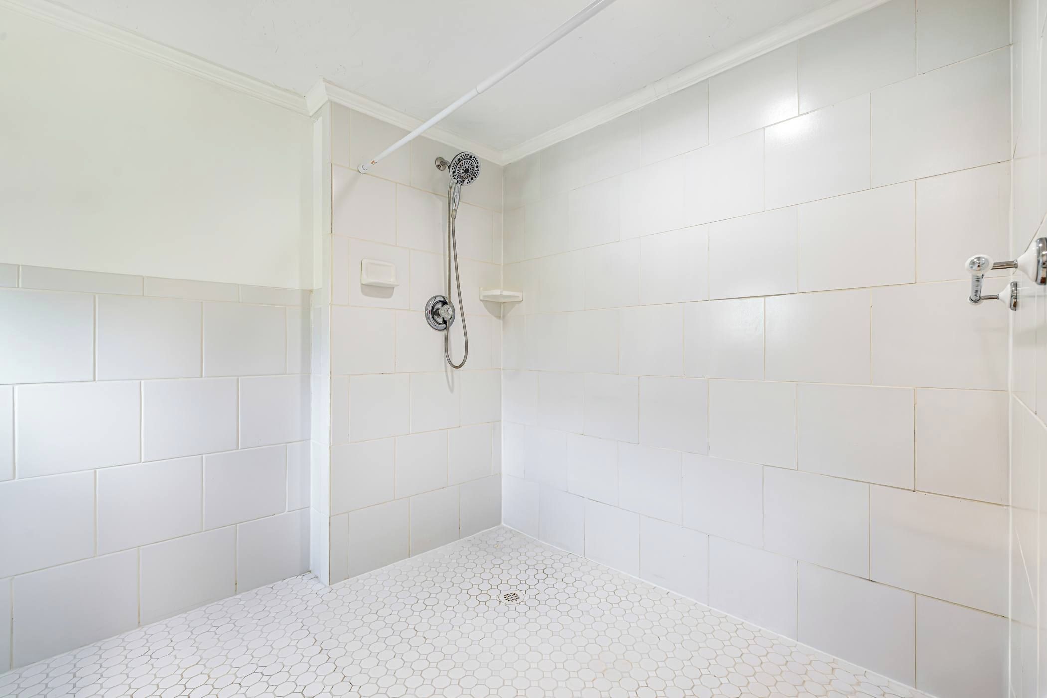 A shower with a handheld showerhead and a wall-mounted faucet.