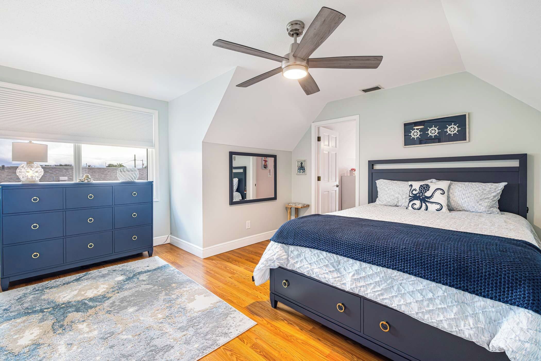 A bedroom with a bed, a dresser, a ceiling fan, and a window with blinds.