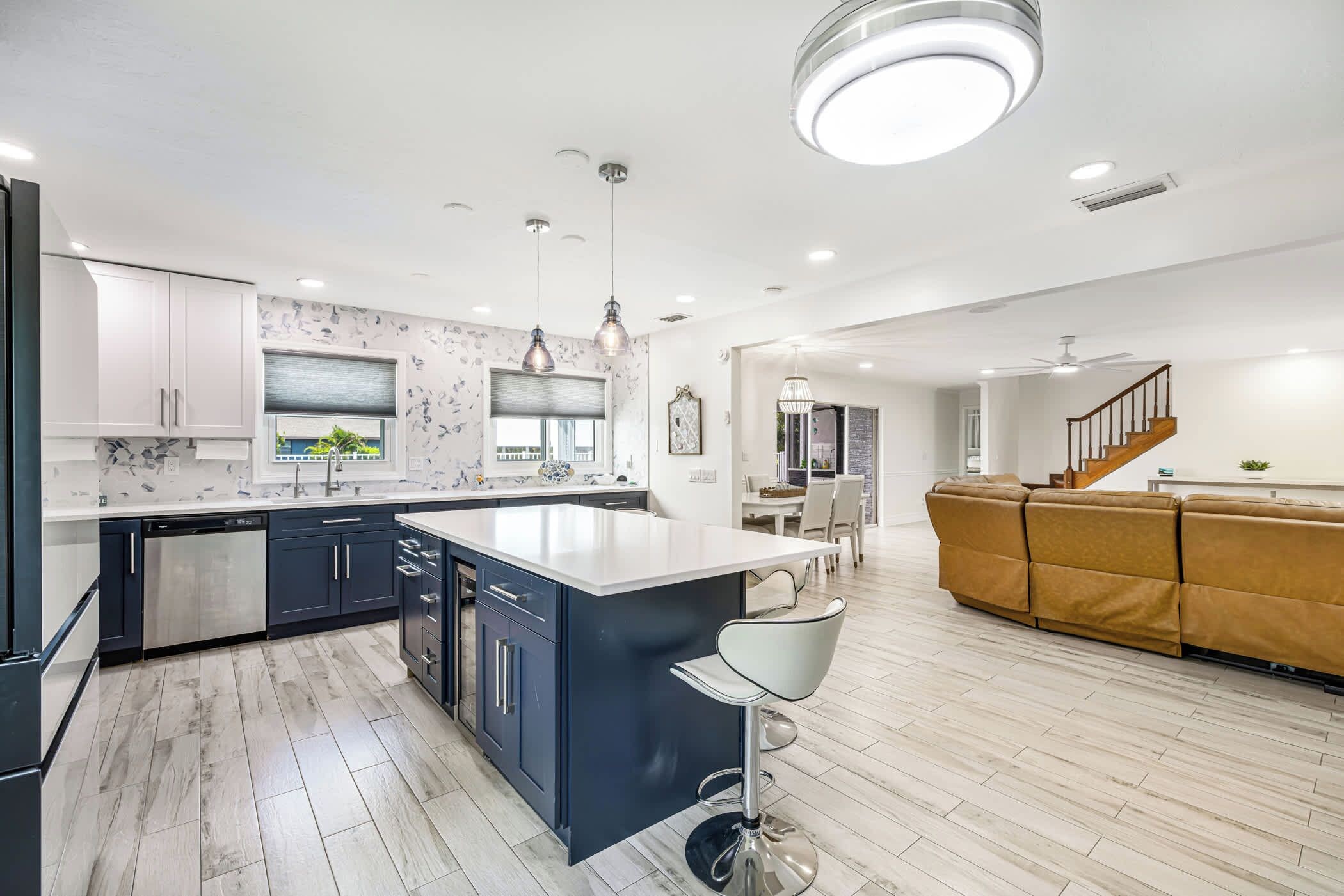A modern kitchen with a central island, dark cabinets, and a dining area with a sofa and table.