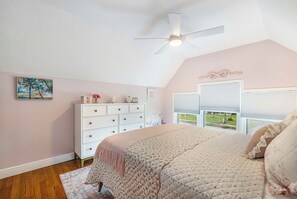 Ein Schlafzimmer mit Bett, Schminktisch, Deckenventilator und einem Fenster mit Jalousien.