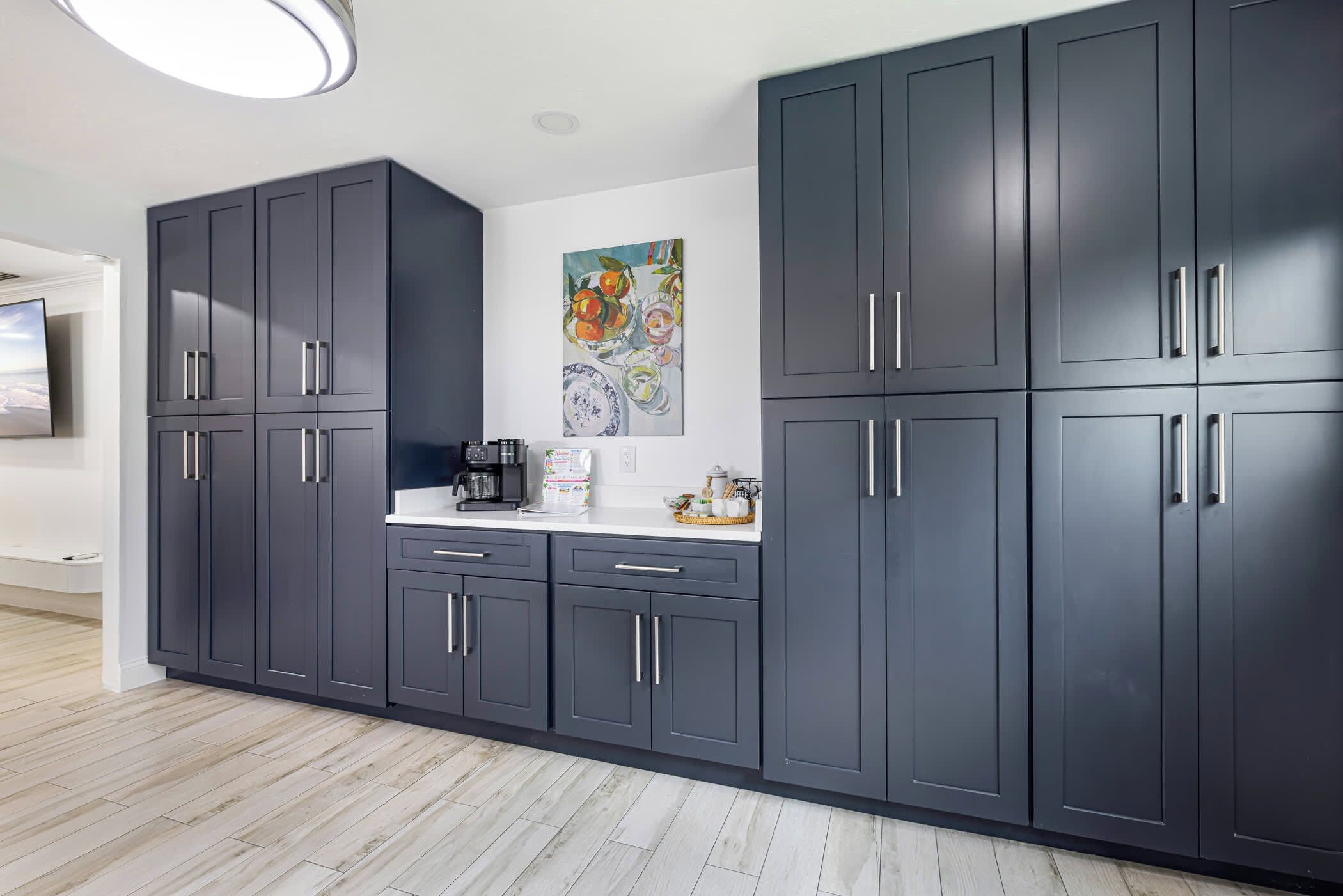 A modern kitchen with dark cabinets, a coffee machine, and a painting on the wall.