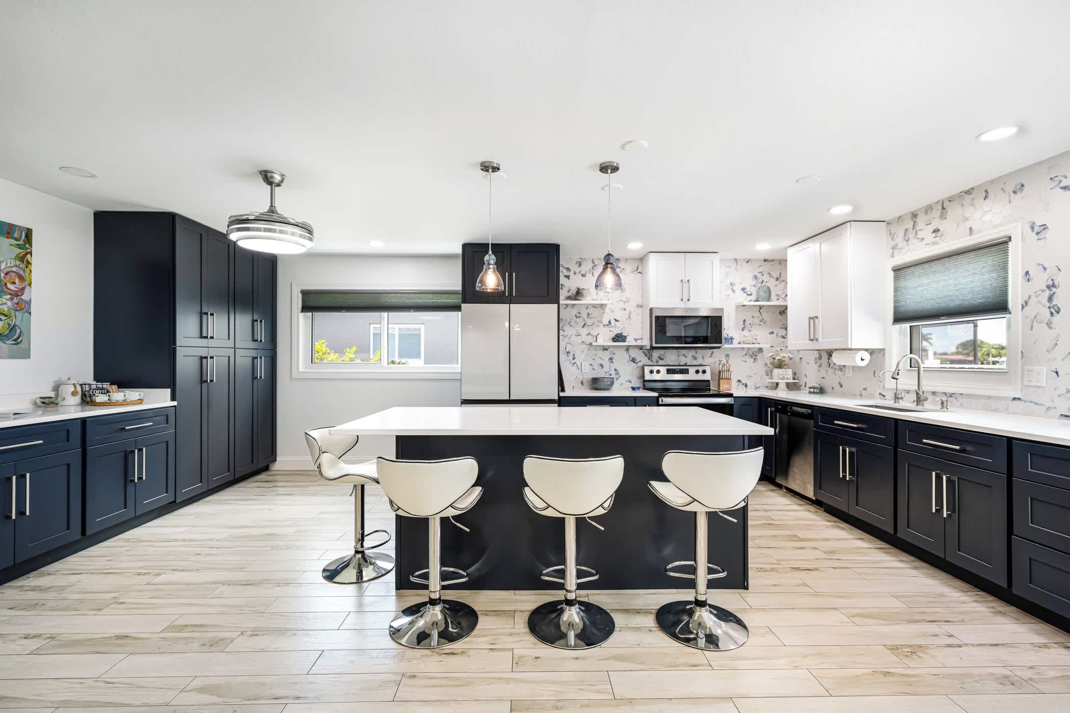 A modern kitchen with a central island, bar stools, a built-in oven, and a large window.
