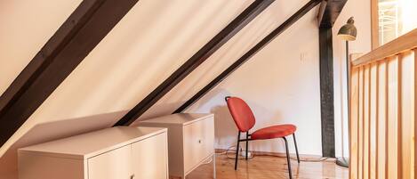 A room with a sloped ceiling, a desk, a chair, and a wardrobe.