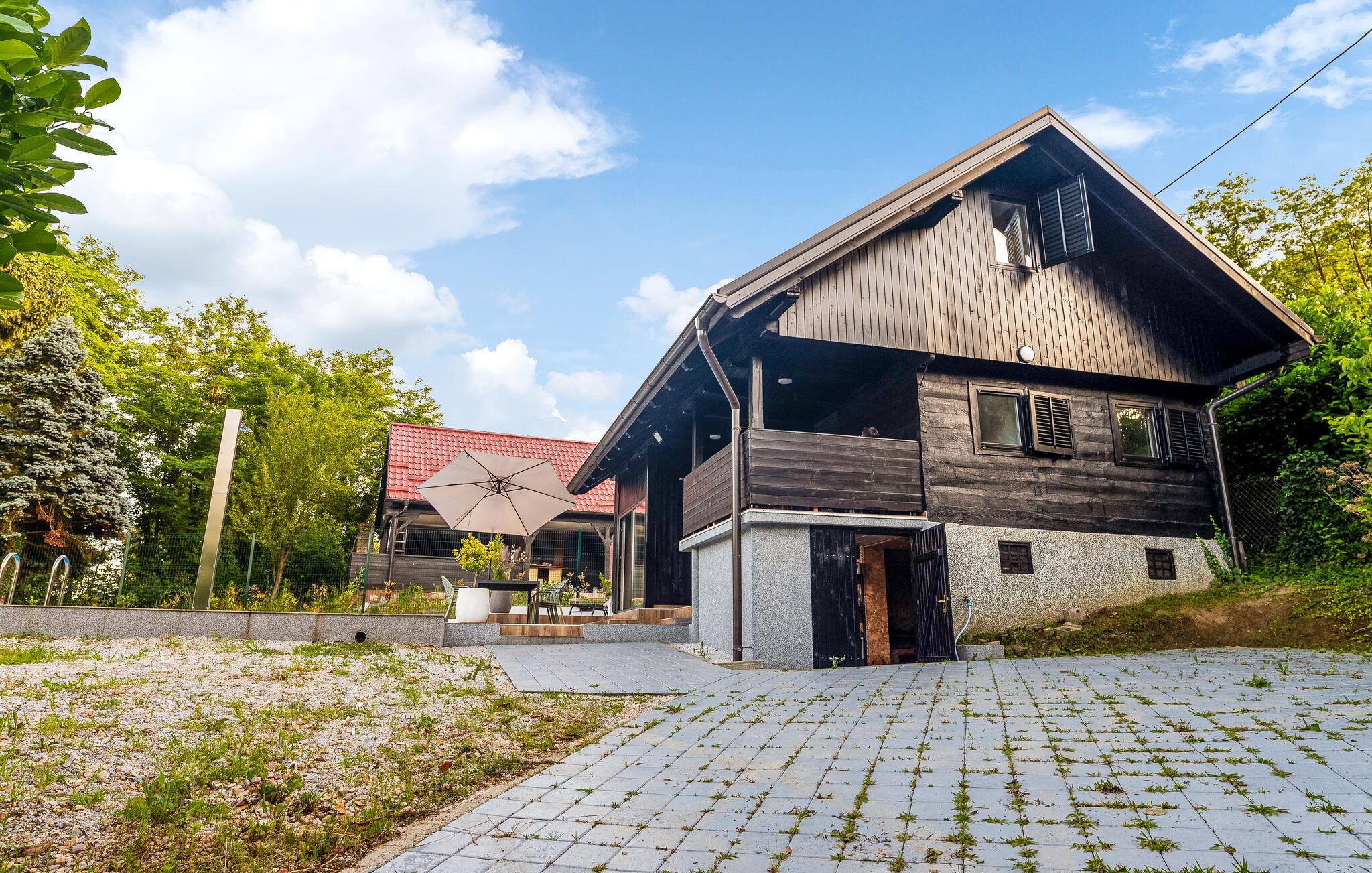 Een houten huis met een schuin dak, een verharde opgang en een tuin met een metalen hek.