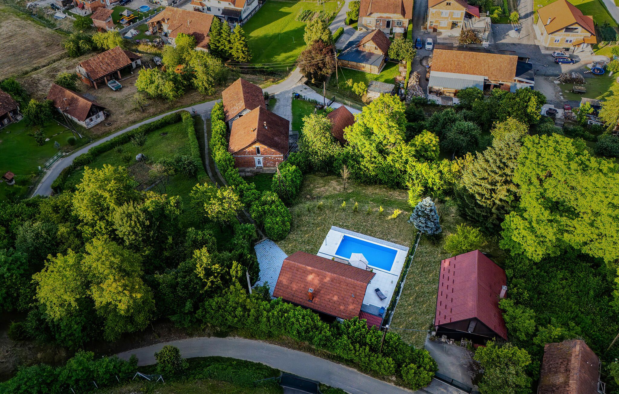An aerial view of a residential area with houses, a swimming pool, and surrounding greenery.