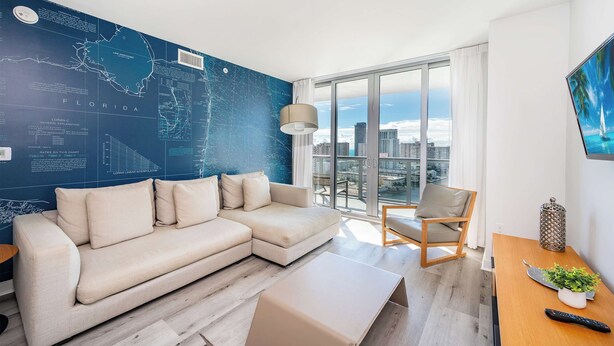 Una sala moderna con un sofá modular, una mesa de centro de madera, vistas a la ciudad a través de amplios ventanales y un mapa en la pared.