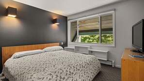 Ein modernes Schlafzimmer mit einem großen Bett, Einbauschränken, einem Fernseher und einem Fenster mit Blick auf Grünflächen.