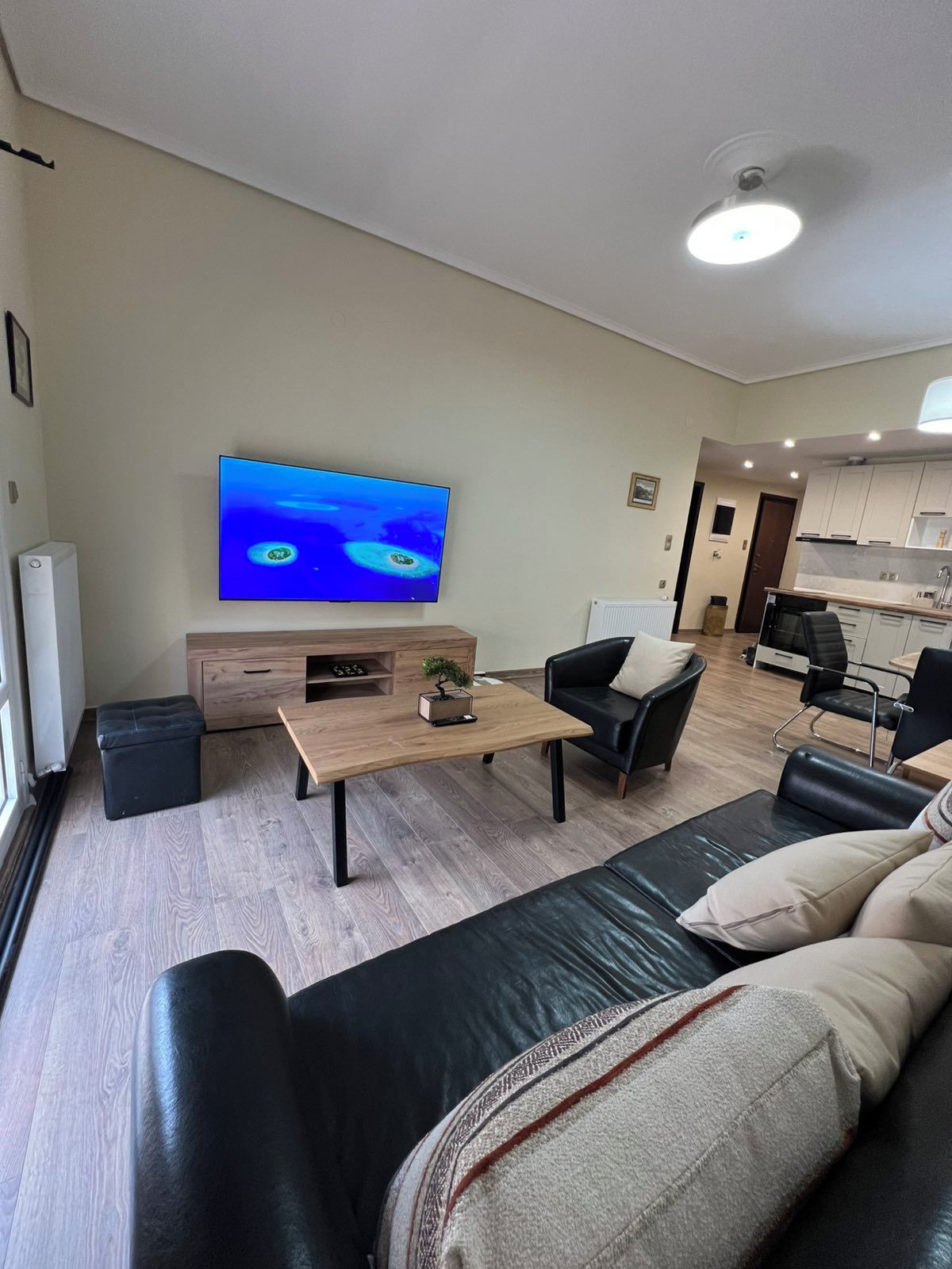 Un soggiorno moderno con una TV a schermo piatto, un tavolino in legno, divani in pelle e un angolo cottura sullo sfondo.
