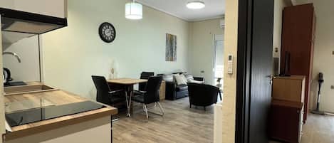 A modern kitchen with a built-in island, dining area with chairs, a clock on the wall, and a ceiling light.