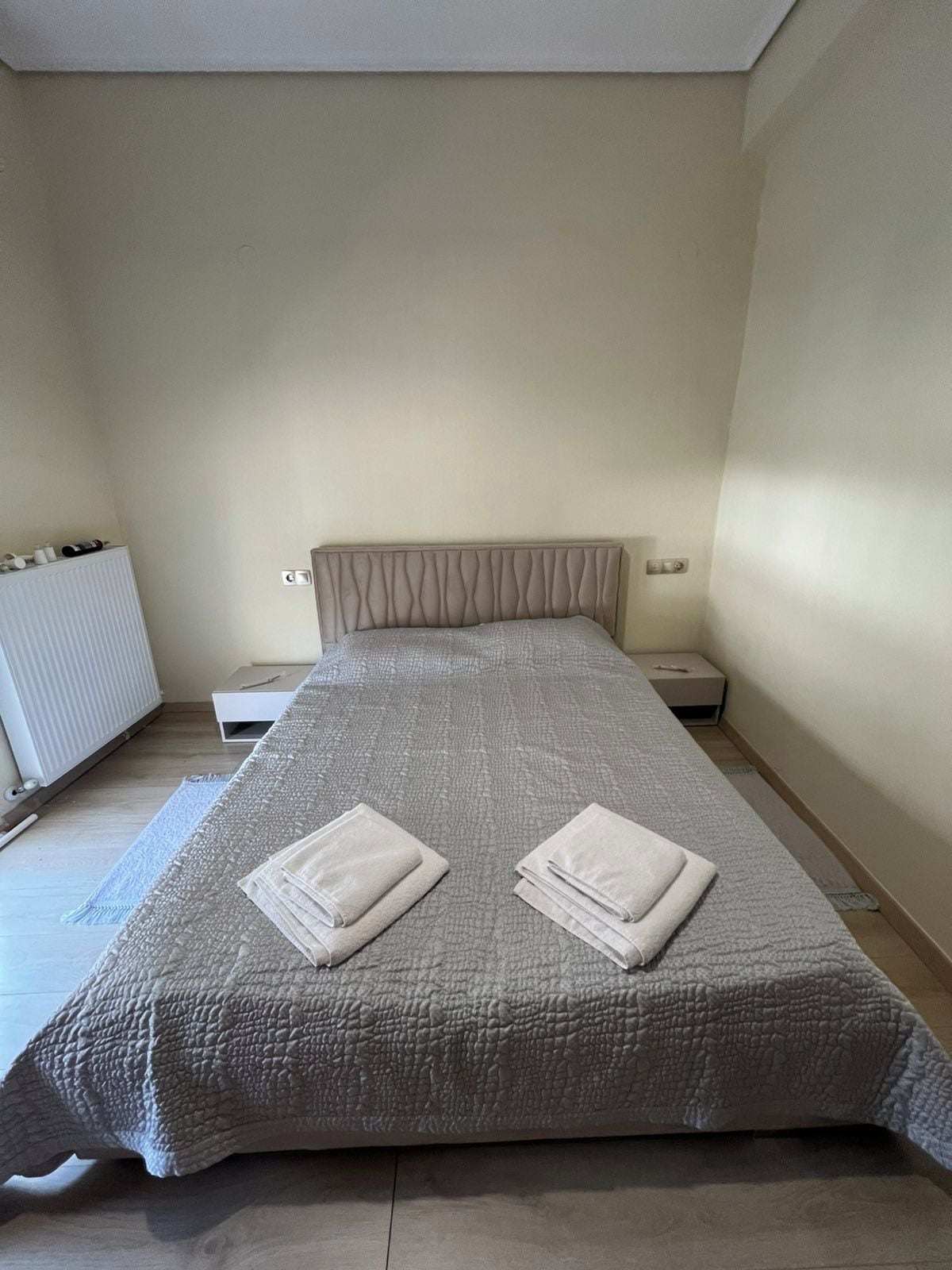 Un dormitorio con cama, mesita de noche, radiador y una pequeña tocador.