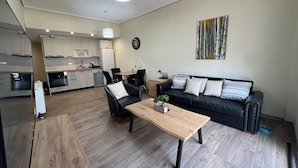Un apartament modern amb zona de menjador, un sofà de cuir negre i una taula de centre de fusta.
