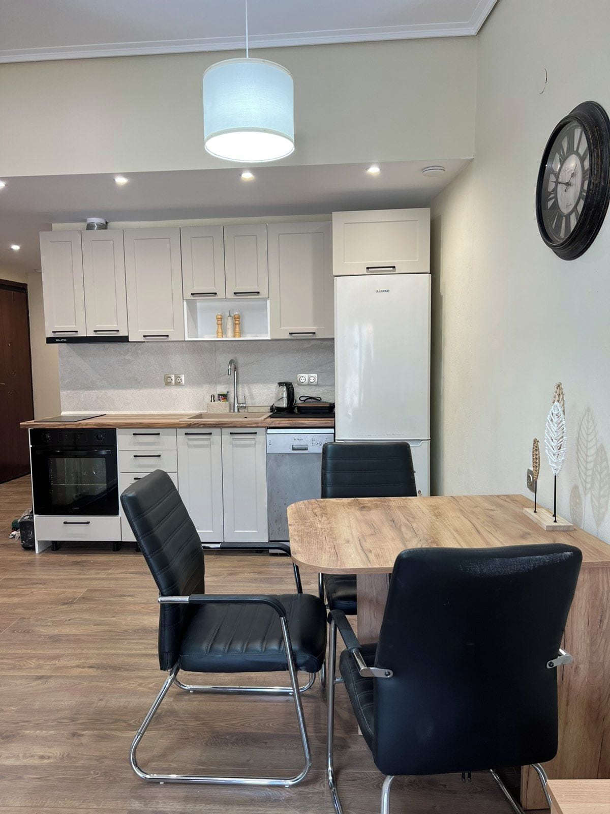 Eine moderne Küche mit weißen Schränken, einer Holz Arbeitsplatte, einem schwarzen Kühlschrank und einem Essbereich mit einem Holztisch und schwarzen Stühlen.