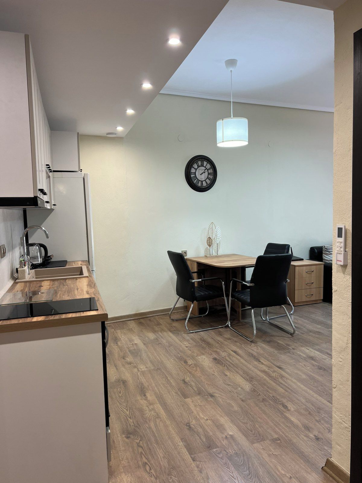 Een moderne keuken met een eethoek, houten vloeren en een klok aan de muur.