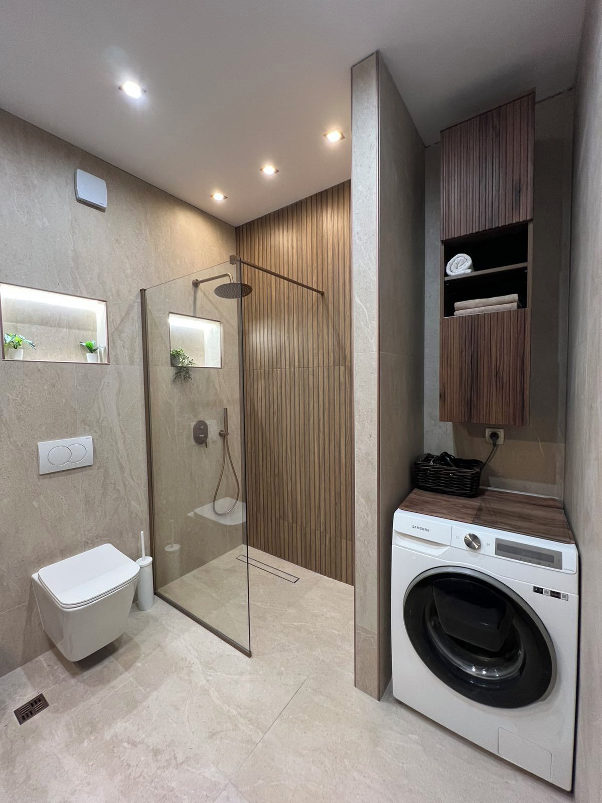 A modern bathroom with a glass-enclosed shower, a toilet, and a built-in washing machine.