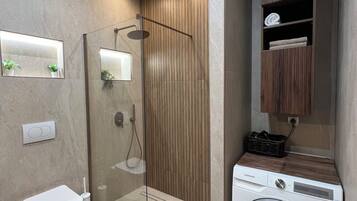 A modern bathroom with a glass-enclosed shower, a toilet, and a built-in washing machine.