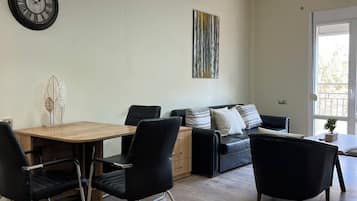 A modern living room with a dining area, featuring a wooden table, black chairs, a black sofa, and a painting on the wall.