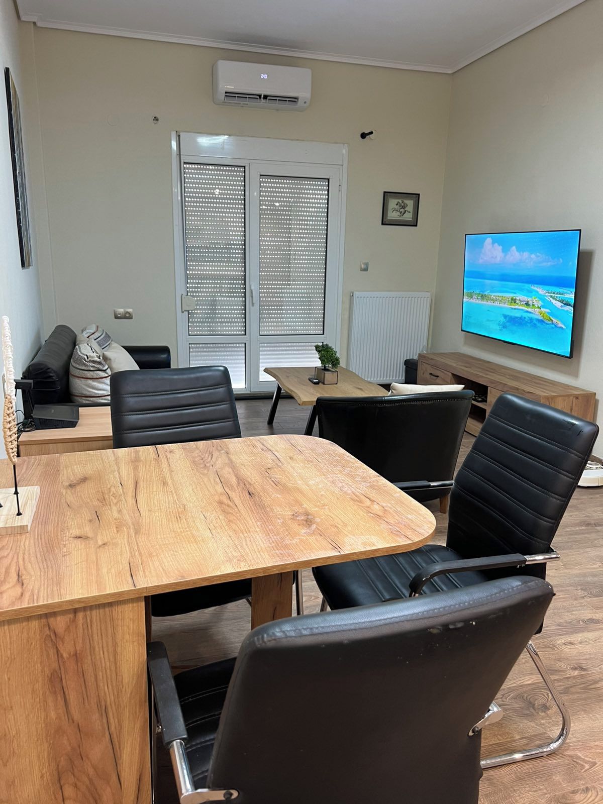 Un salón de conferencias con una mesa de madera, sillas negras, un sofá y un televisor que muestra una vista panorámica.