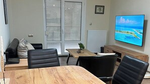 Una sala de conferències amb taula de fusta, cadires negres, un sofà i una televisió que mostra un paisatge idíl·lic.