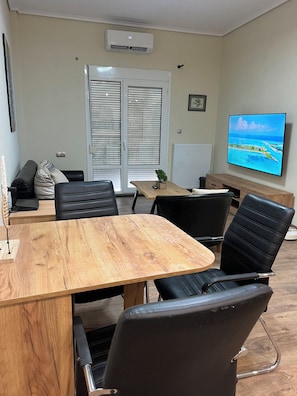 Un salón de conferencias con una mesa de madera, sillas negras, un sofá y un televisor que muestra una vista panorámica.